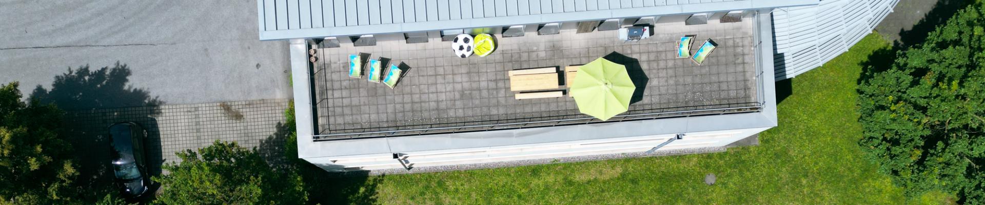 Die Dachterrasse des SOCCA GROUP Headquarters in Rosenheim, ausgestattet mit Liegestühlen, Sitzbänken und einem Sonnenschirm bietet eine entspannte Atmosphäre.