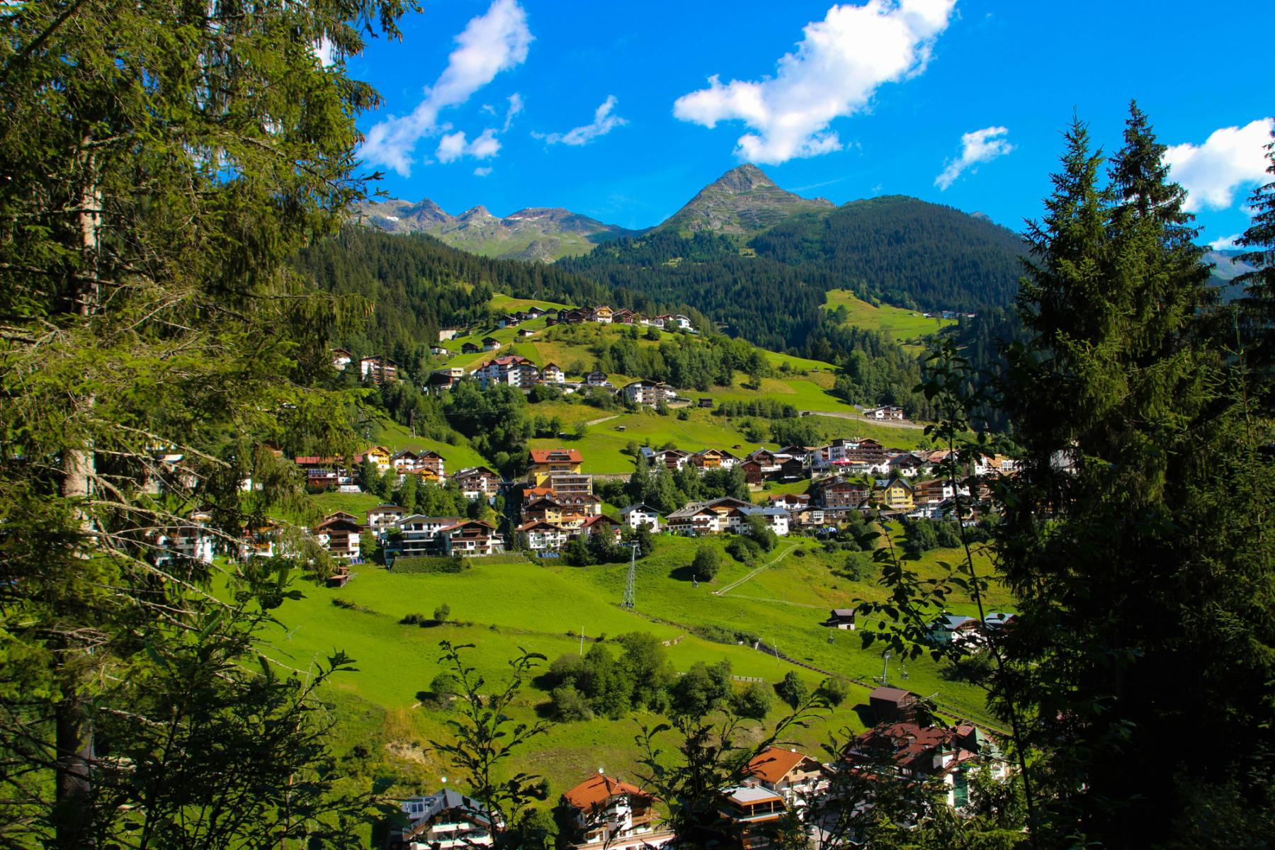 Malerisches Bergdorf in Österreich, umgeben von grünen Wiesen, Wäldern und Bergen unter blauem Himmel