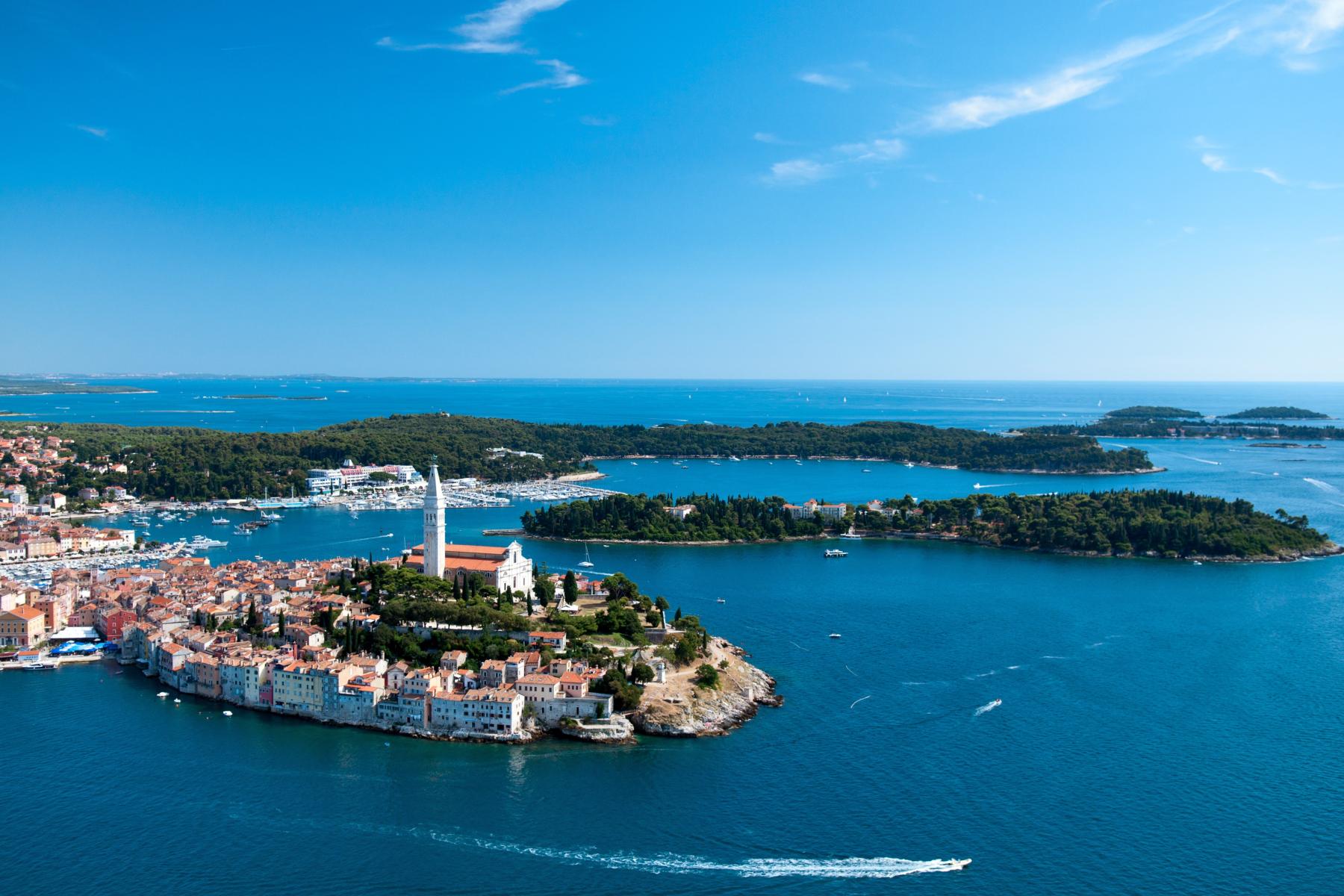 Luftaufnahme einer Küstenstadt in Kroatien mit Kirche, Glockenturm und umliegenden Inseln im blauen Meer