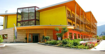 Sand-Tennisplatz mit Spielern, Hotel im Hintergrund und Bergkulisse.